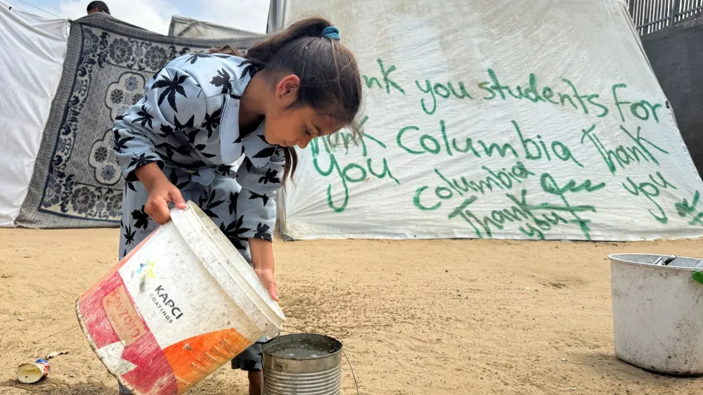 A girl pours water next to a tent sprayed with a message thanking pro-Palestinian university students who are protesting for their support, amid the ongoing conflict between Israel and Palestinians, in Rafah in the southern Gaza Strip, May 2, 2024. REUTERS/Mohammed Salem