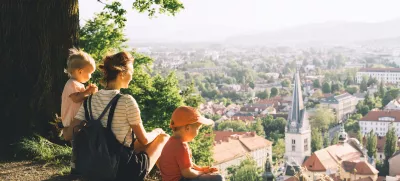 Family on background of Ljubljana, Slovenia, Europe. Woman with two little children looks at panorama of european city from the hill. Mother and kids outdoors at spring or summer time. / Foto: Nataliaderiabina