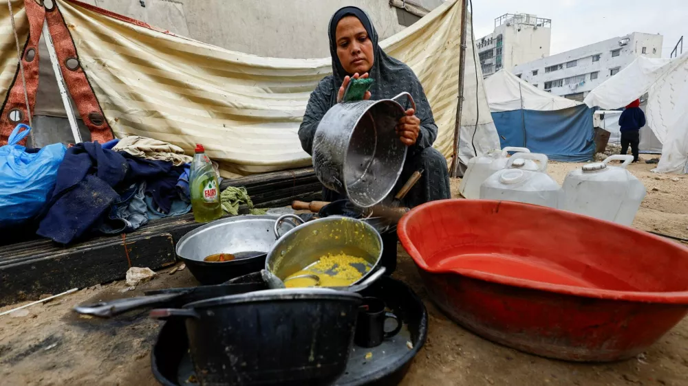 A displaced Palestinian woman washes kitchen items outside her tent, amid a ceasefire between Israel and Hamas, in Gaza City, November 4, 2025. REUTERS/Mahmoud Issa