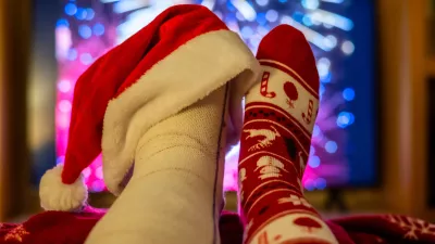 Watching colorful fireworks on tv while relaxing at home, feet up and adorned with a festive christmas sock and a santa hat on a broken foot, celebrating the new year with humor and warmth / Foto: Nanci Santos, Getty Images