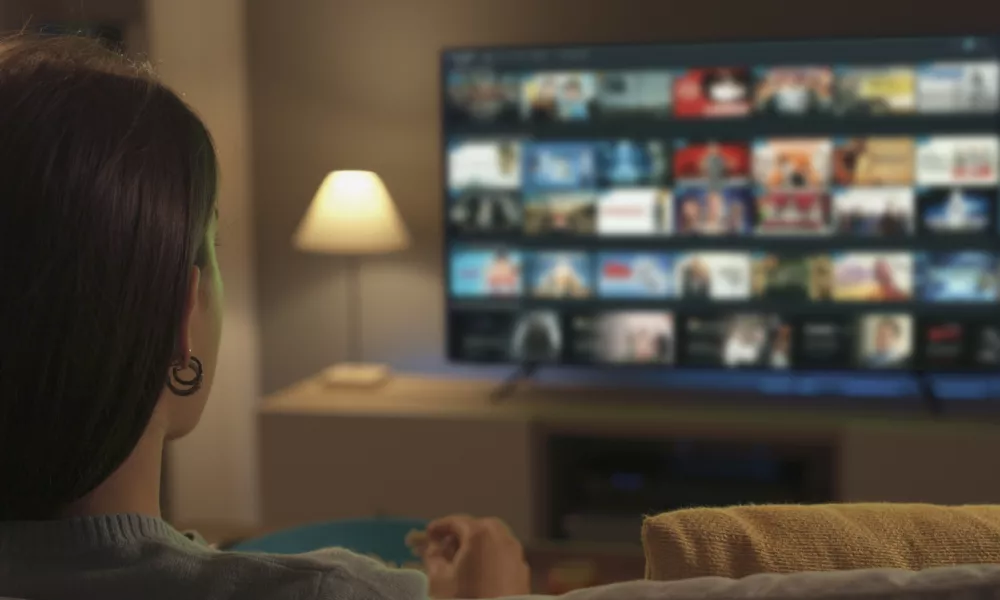 Young woman relaxing on the couch at home and watching videos on demand on her TV, entertainment concept