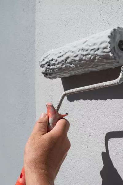 Painter's hand holding a roller filled with paint to paint an exterior wall / Foto: Leirao, Getty Images