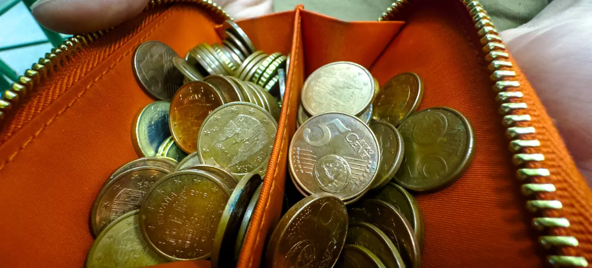 Close-up view of an unzipped orange wallet brimming with assorted euro cent coins, symbolizing budgeting, savings, and small change handling. / Foto: Pavel Samsonov, Getty Images