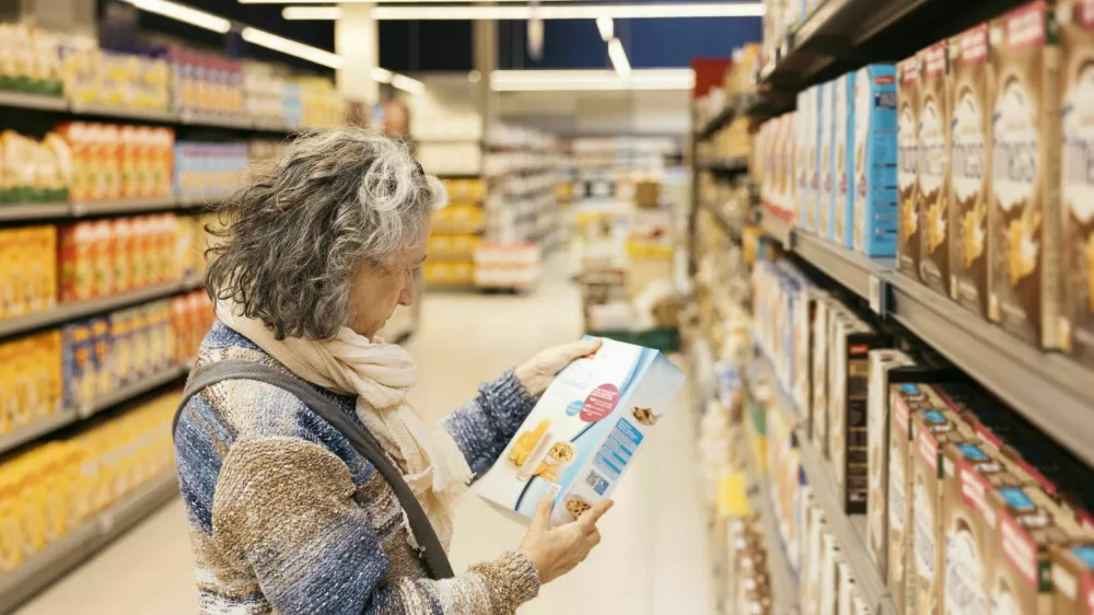 Senior adult woman reading product information on a cereal box while shopping at the grocery store / Foto: Jordi Salas