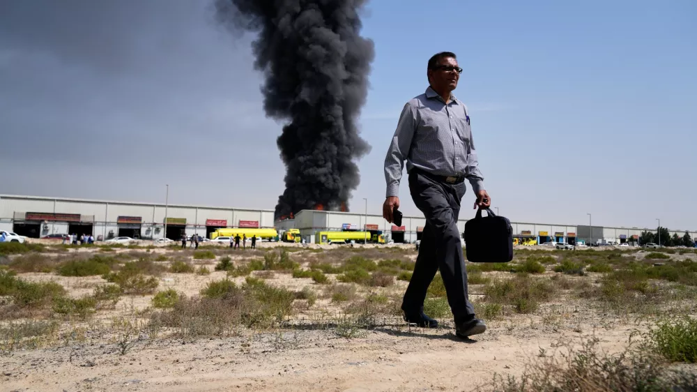 A man walks away after watching as a black plume of smoke rises from a warehouse in the industrial area of Sharjah City, United Arab Emirates, Sunday, March 1, 2026, following reports of Iranian strikes in Dubai. (AP Photo/Altaf Qadri)