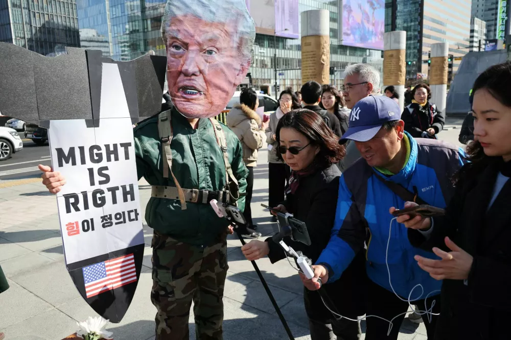 People film next to an activist wearing a cutout mask depicting U.S. President Donald Trump, during a rally to condemn the joint U.S.&ndash;Israel strikes on Iran, amid the U.S.-Israel conflict with Iran, in front of the U.S. embassy in Seoul, South Korea, March 3, 2026.  REUTERS/Kim Hong-Ji
