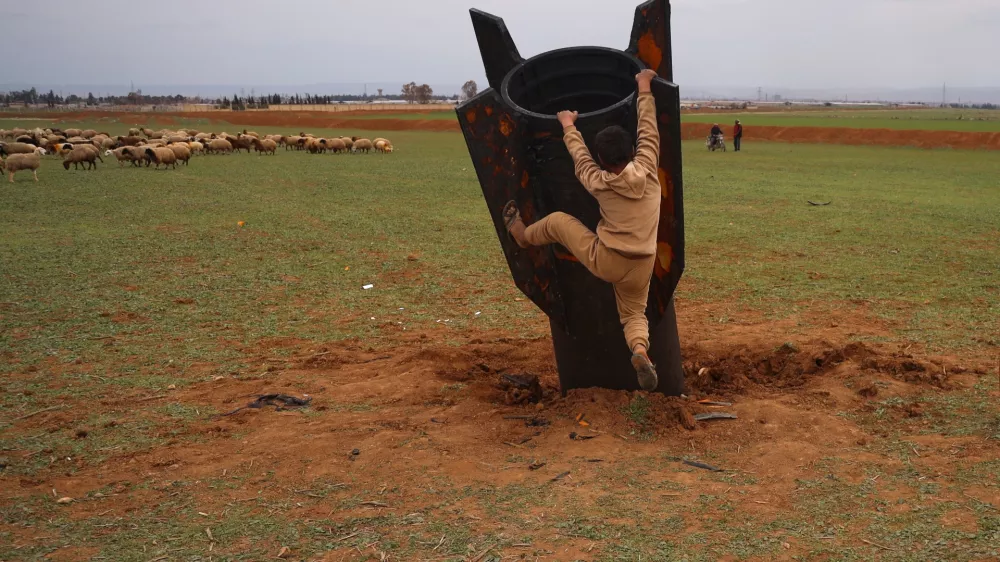 Exposing himself to the danger of unexploded ordnance, a boy tries to climb on an unexploded Iranian projectile that landed in an open field in the outskirts of Qamishli, eastern Syria, Wednesday, March 4, 2026.(AP Photo/Baderkhan Ahmad)