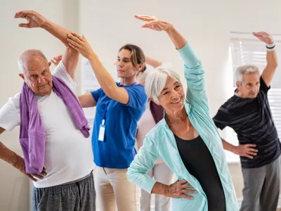Active seniors doing exercise with physiotherapist at nursing home gym. Trainer helping elderly man and old woman exercising at home. Retired people doing stretching exercises at retirement community.