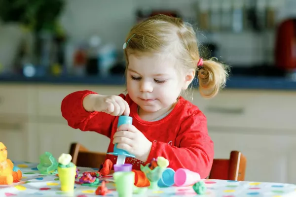 Adorable cute little toddler girl with colorful clay. Healthy baby child playing and creating toys from play dough. Small kid molding modeling clay and learning.