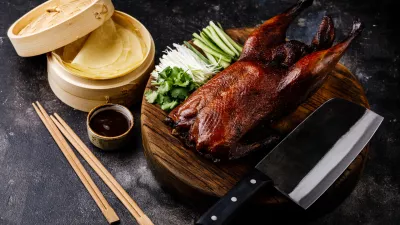 Peking Duck set with fresh cucumber, onion, Hoysin sauce, pancakes and Cleaver on wooden cutting board on dark background / Foto: Lisovskaya