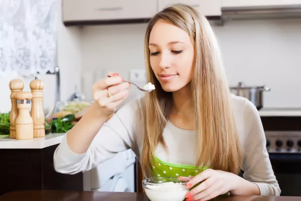 Blonde woman eating curd cheese in home kitchen / Foto: Jackf