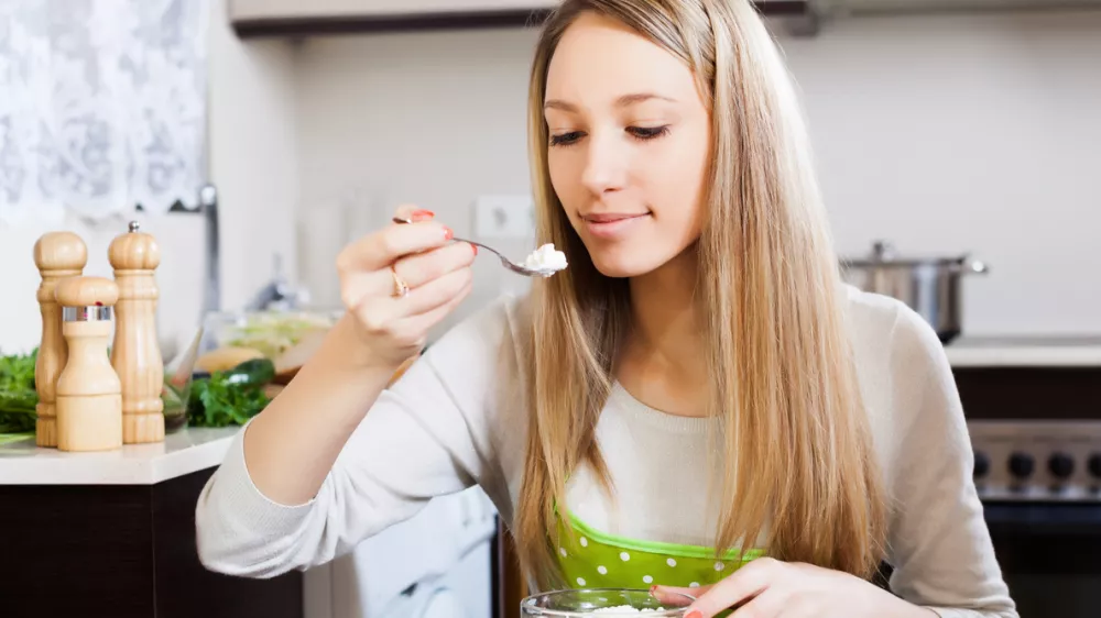 Blonde woman eating curd cheese in home kitchen / Foto: Jackf