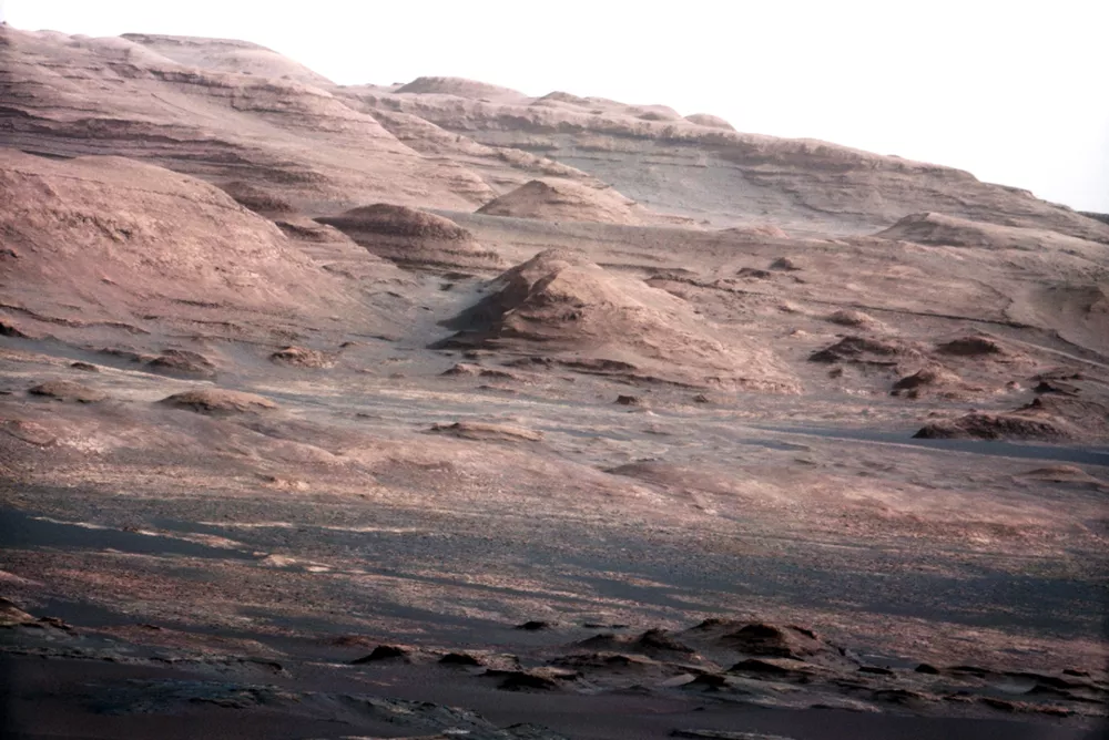 In this image released by NASA on Monday, Aug. 27, 2012, a chapter of the layered geological history of Mars is laid bare in this color image from NASA's Curiosity rover showing the base of Mount Sharp, the rover's eventual science destination. The image is a portion of a larger image taken by Curiosity's 100-millimeter Mast Camera on Aug. 23, 2012. Scientists enhanced the color in one version to show the Martian scene under the lighting conditions we have on Earth, which helps in analyzing the terrain. The pointy mound in the center of the image, looming above the rover-sized rock, is about 1,000 feet (300 meters) across and 300 feet (100 meters) high. (AP Photo/NASA/JPL-Caltech/MSSS)
