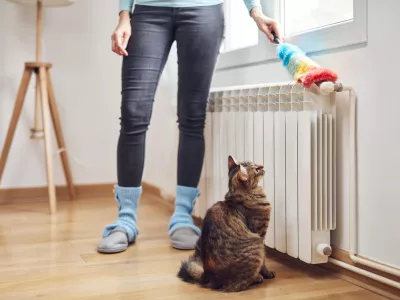 Woman with a dust stick cleaning central heating gas radiator at home. / Foto: M-gucci