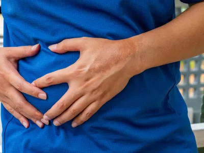 Man clutching abdomen in pain&mdash;possible liver-related symptoms such as hepatic inflammation, cirrhosis, or bile duct disorder. Liver disease, abdominal pain, hepatology. / Foto: Prasert Kunanuphanchai