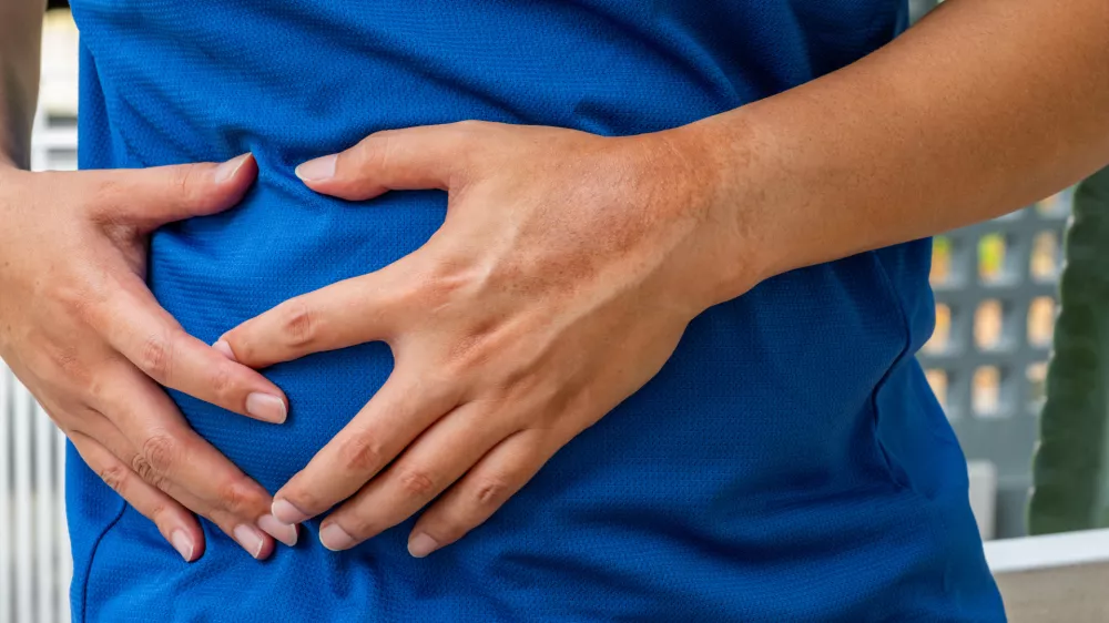 Man clutching abdomen in pain&mdash;possible liver-related symptoms such as hepatic inflammation, cirrhosis, or bile duct disorder. Liver disease, abdominal pain, hepatology. / Foto: Prasert Kunanuphanchai