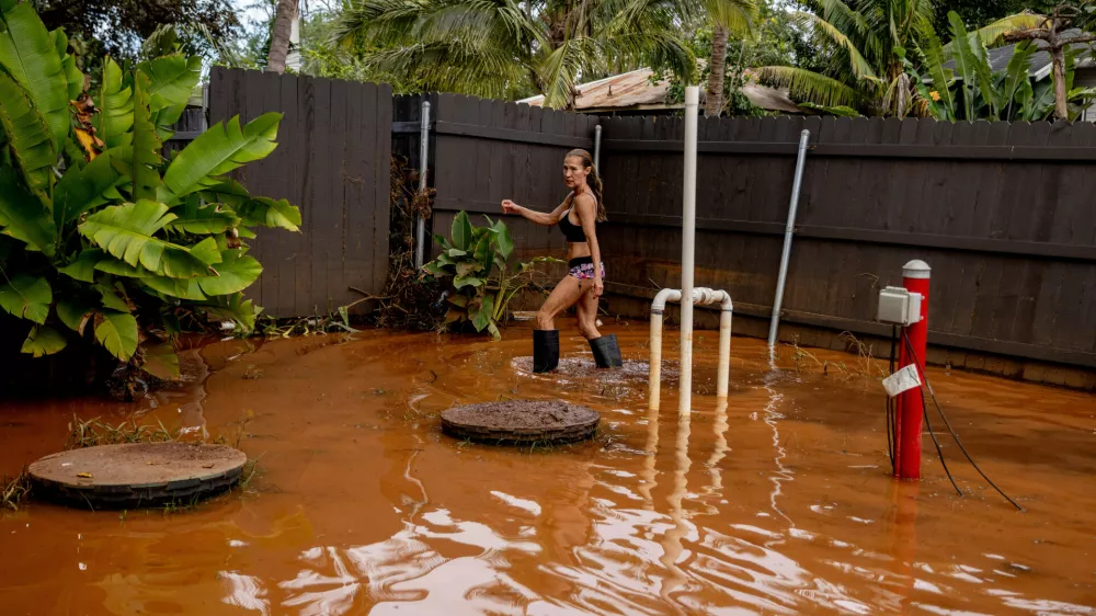 Linda Griffith wades through a flooded yard in Haleiwa, Hawaii Saturday, March 21, 2026. (Stephen Lam/San Francisco Chronicle via AP)
