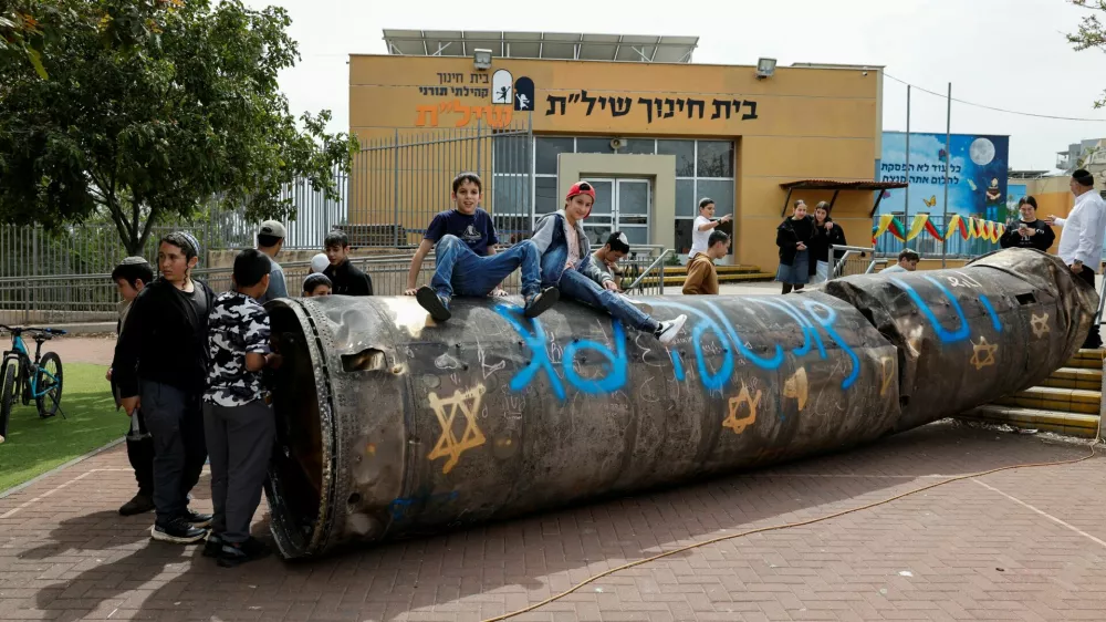 Children and teenagers play with a part of a missile that landed in the playground of an elementary school last night, amid the U.S.-Israel conflict with Iran, in the Israeli settlement Peduel of the Israel-occupied West Bank, March 23, 2026. REUTERS/Amir Cohen   TPX IMAGES OF THE DAY