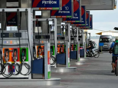 A motorcycle rider enters a gasoline station while a bicycle passes by on Wednesday, March 25, 2026, in Paranaque city, Philippines. (AP Photo/Aaron Favila)