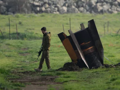 FILE - An Israeli soldier stands next to a fragment of a missile fired from Iran and intercepted by Israeli air defense system embedded in an open field in the Israeli-controlled Golan Heights, March 19, 2026. (AP Photo/Ohad Zwigenberg, File)