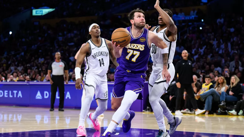 Mar 27, 2026; Los Angeles, California, USA; Los Angeles Lakers guard Luka Doncic (77) drives against Brooklyn Nets guards Ochai Agbaji (30) and Terance Mann (14) during the second half at Crypto.com Arena. Mandatory Credit: William Liang-Imagn Images