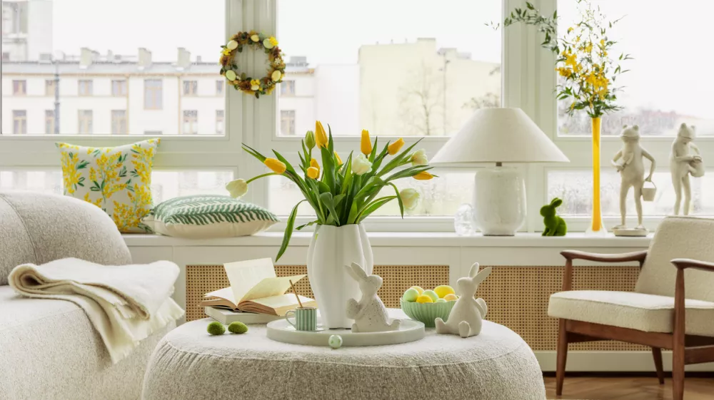 Bright living room with an Easter setup featuring yellow tulips in a white vase, soft textured pillows, and delicate decorations, creating a warm and festive ambiance.