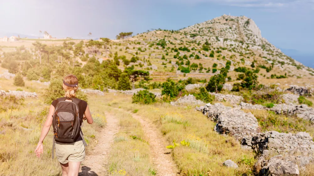 Young woman with backpack at mountain trail. Sveti Nikola mount, Hvar Island, Croatia