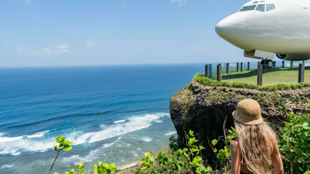 Blonde tourist admiring repurposed boeing 737 airplane on a cliff overlooking the indian ocean in bali,Image: 1001085464, License: Royalty-free, Restrictions:, Model Release: yes