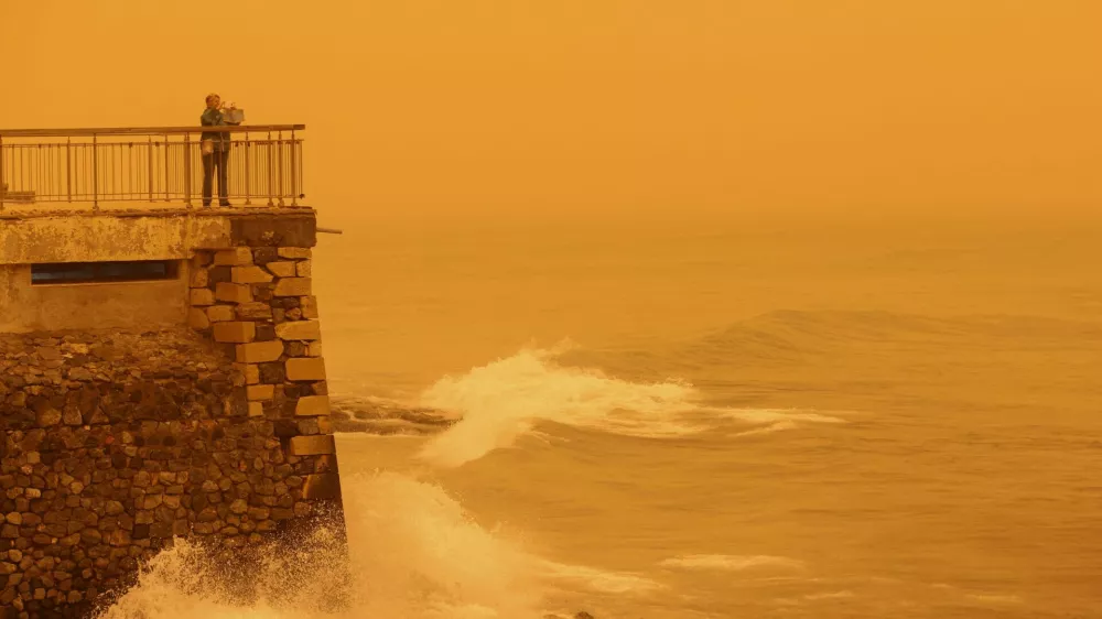 A woman takes pictures of the horizon turned yellow, caused by sand dust from the Sahara, due to strong southern winds, in Heraklion, Crete island, Greece April 1, 2026. REUTERS/Stefanos Rapanis