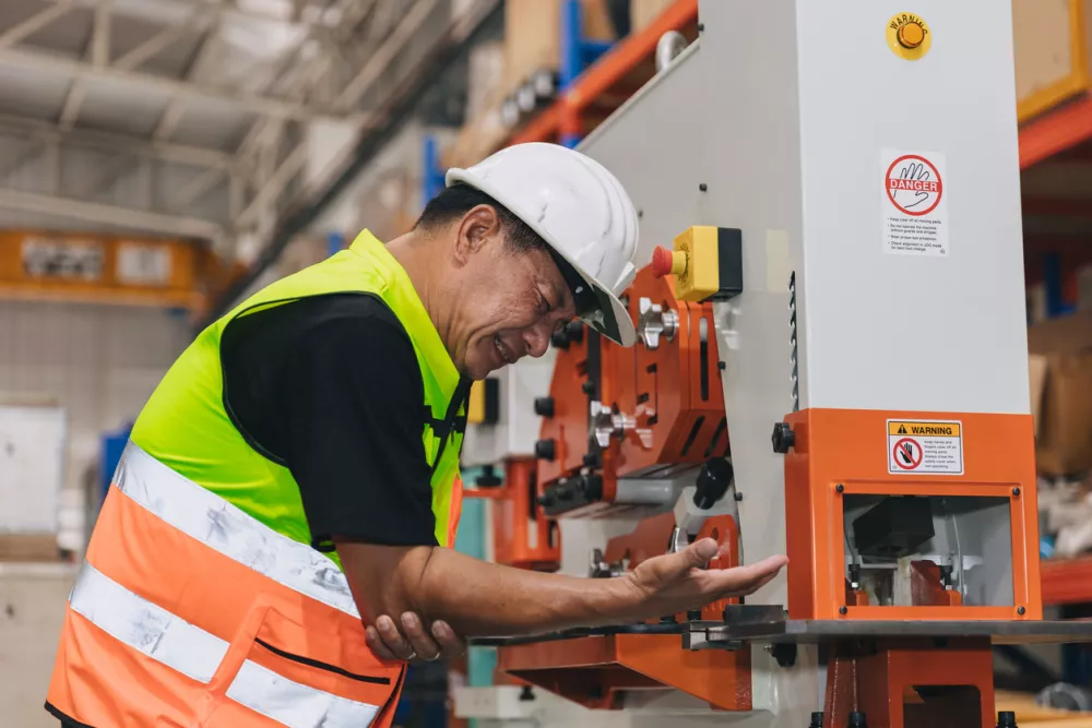 Senior male worker serious accident machine hand clamp injury in industry workplace need emergency medical help / Foto: Coffeekai Getty Images