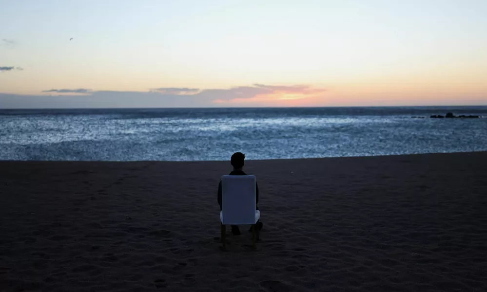 A tourist sits on a chair and looks out at sunrise on a beach in Barcelona, Spain, February 12, 2026. REUTERS/Nacho Doce / Foto: Nacho Doce