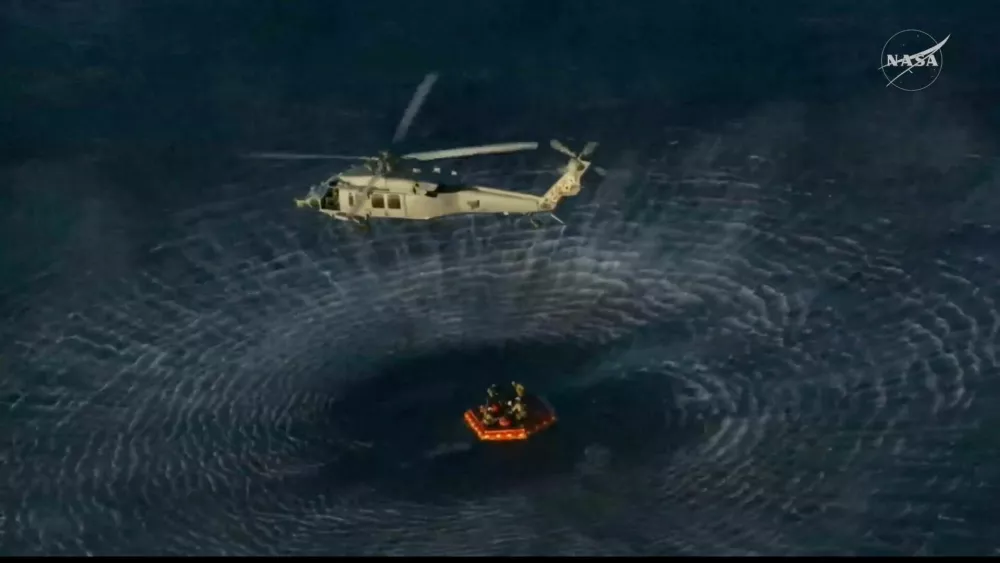 A helicopter awaits to transport a crew member to the recovery ship after being extracted from the Artemis II capsule by recovery personnel in the Pacific Ocean in this screengrab from a livestream video after the Artemis II crew's flyby of the Moon, April 10, 2026. NASA/Handout via REUTERS THIS IMAGE HAS BEEN SUPPLIED BY A THIRD PARTY
