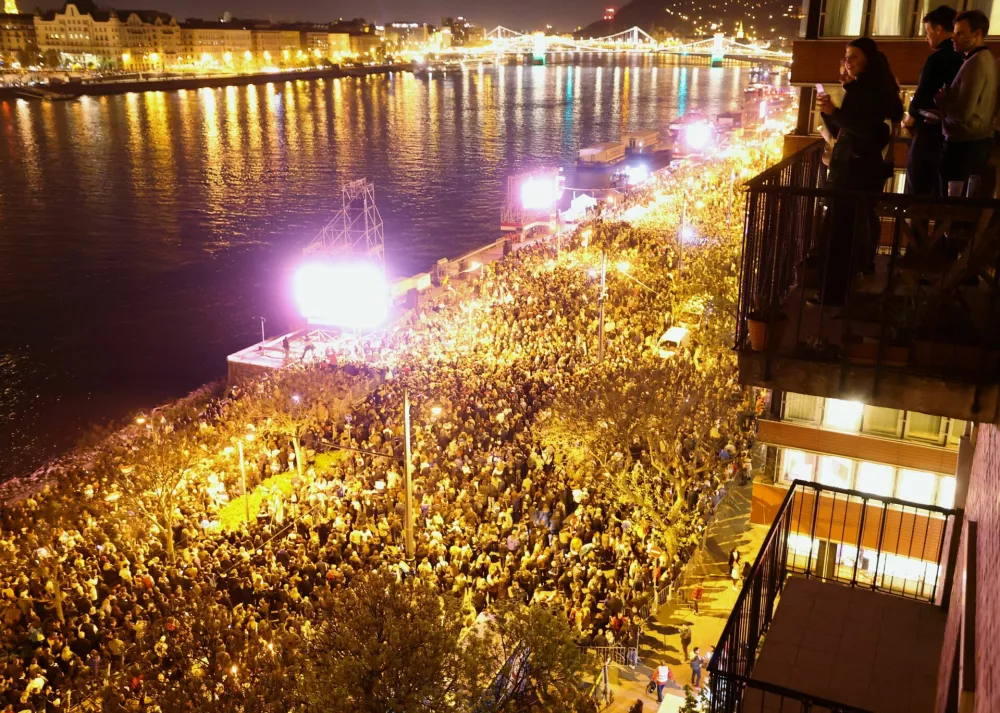 People look from a balcony during a celebration across the River Danube from the Parliament building, following the partial results of the parliamentary election, in Budapest, Hungary, April 12, 2026. REUTERS/Lisi Niesner