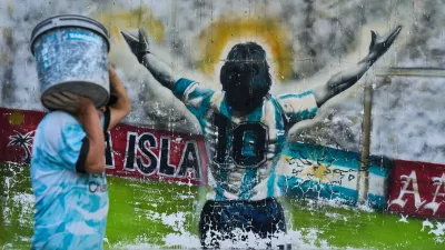 A pedestrian carries a bucket past graffiti depicting late soccer legend Diego Maradona in Buenos Aires, Argentina, Monday, April 13, 2026. (AP Photo/Rodrigo Abd)