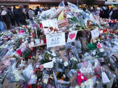 FILE - People stand around floral tributes and candles placed outside the sealed off Le Constellation bar in Crans-Montana, Swiss Alps, Switzerland, on Jan. 3, 2026, where a devastating fire left dead and injured during the New Year's celebrations. (AP Photo/ Antonio Calanni, File)