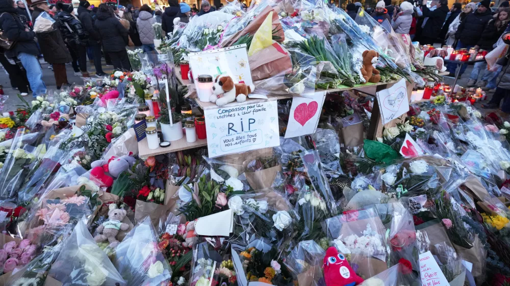 FILE - People stand around floral tributes and candles placed outside the sealed off Le Constellation bar in Crans-Montana, Swiss Alps, Switzerland, on Jan. 3, 2026, where a devastating fire left dead and injured during the New Year's celebrations. (AP Photo/ Antonio Calanni, File)