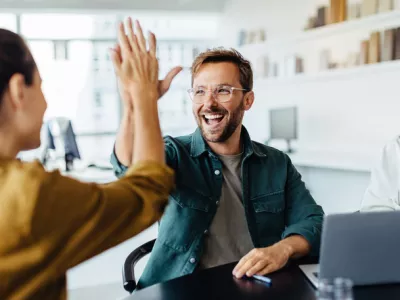 Successful business people giving each other a high five in a meeting. Two young business professionals celebrating teamwork in an office.