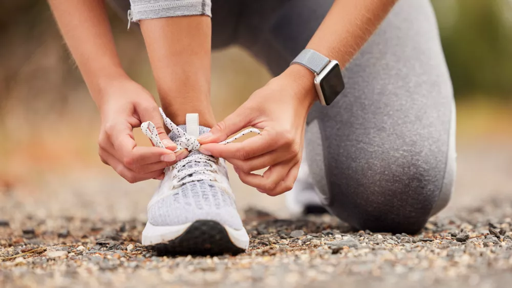 Shoes, fitness and exercise with a sports woman tying her laces before training, running or a workout. Hands, health and cardio with a female runner or athlete getting ready for an endurance run