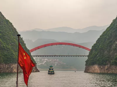 Wushan, Chongqing, China - May 7, 2010: Wu Gorge in Yangtze River. Red S103 road bow bridge over Daning River at connection with green Yangtze. Chinese flag and boat. Mountains on horizon.