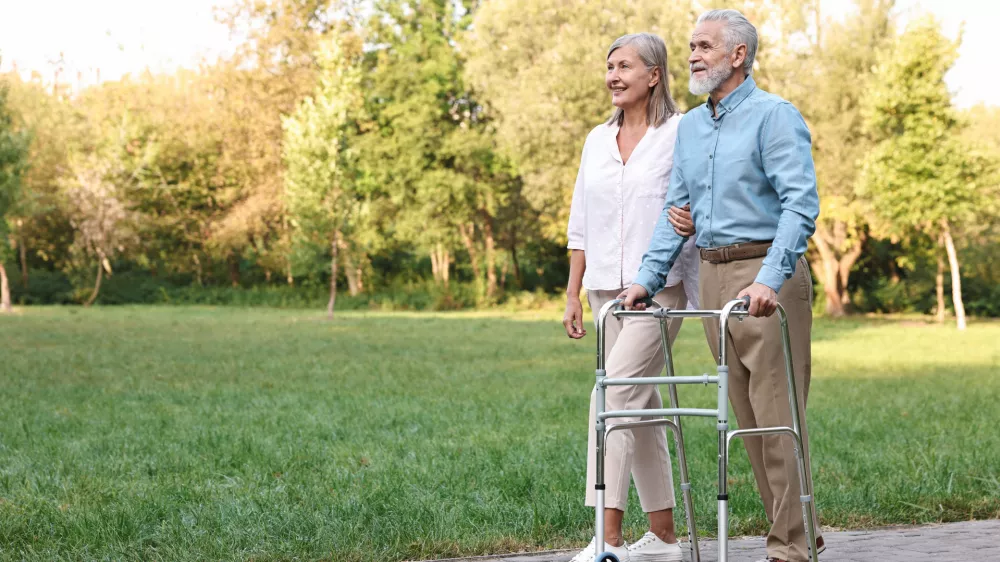 Senior couple with walking frame in park, space for text / Foto: Olga Yastremska
