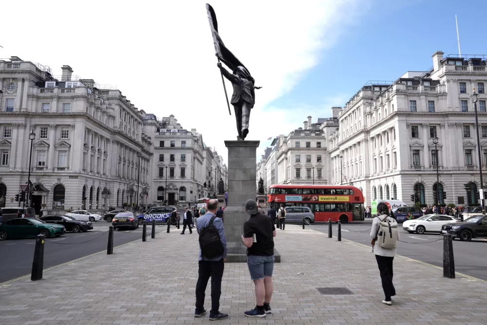 Members of the public look at a statue of a man holding a flag which covers their face, and signed 'Banksy', has appeared in Waterloo Place in London. (Stefan Rousseau/PA via AP)