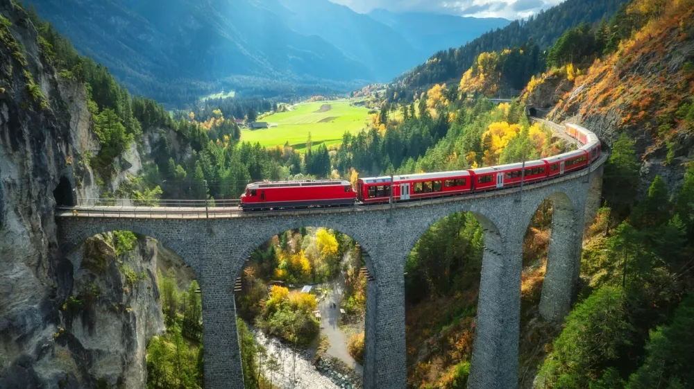 Aerial view of modern red train on Landwasser viaduct in alpine mountains, colorful forest at sunset in autumn. Bernina Express, Switzerland. Top view of train in Alps, railroad, green trees in fall,Image: 1003820041, License: Royalty-free, Restrictions:, Model Release: yes