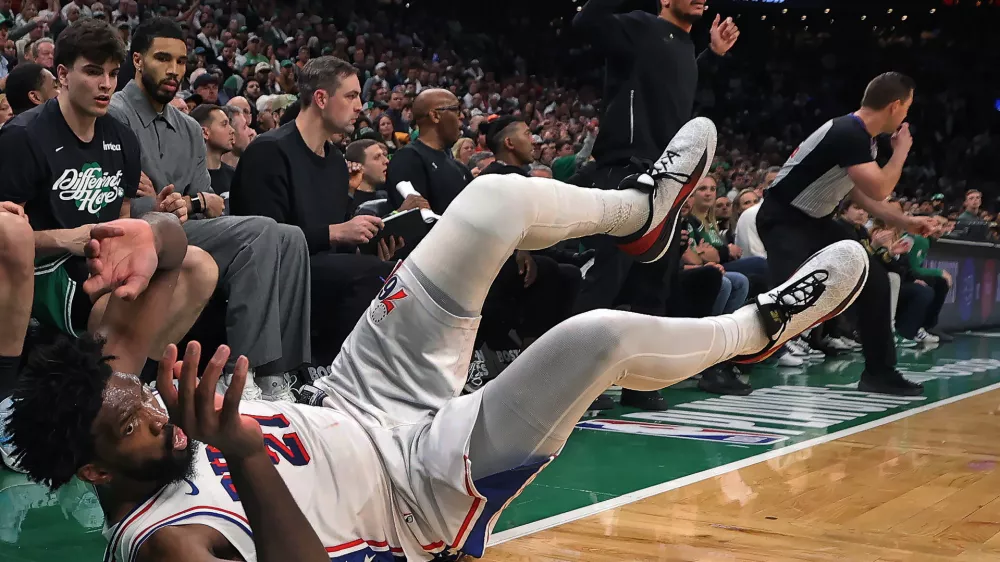 Philadelphia 76ers' Joel Embiid dives onto the ground in pursuit of a loose ball in front of the Boston Celtics bench late in the fourth quarter. Celtics head Joe Mazzulla is standing in the center, while injured Celtics player Jayson Tatum (in grey at left) looks on during Game 7 of a first round NBA basketball playoffs series, Saturday, May 2, 2026 in Boston. (AP Photo/Jim Davis)