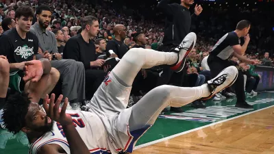 Philadelphia 76ers' Joel Embiid dives onto the ground in pursuit of a loose ball in front of the Boston Celtics bench late in the fourth quarter. Celtics head Joe Mazzulla is standing in the center, while injured Celtics player Jayson Tatum (in grey at left) looks on during Game 7 of a first round NBA basketball playoffs series, Saturday, May 2, 2026 in Boston. (AP Photo/Jim Davis)