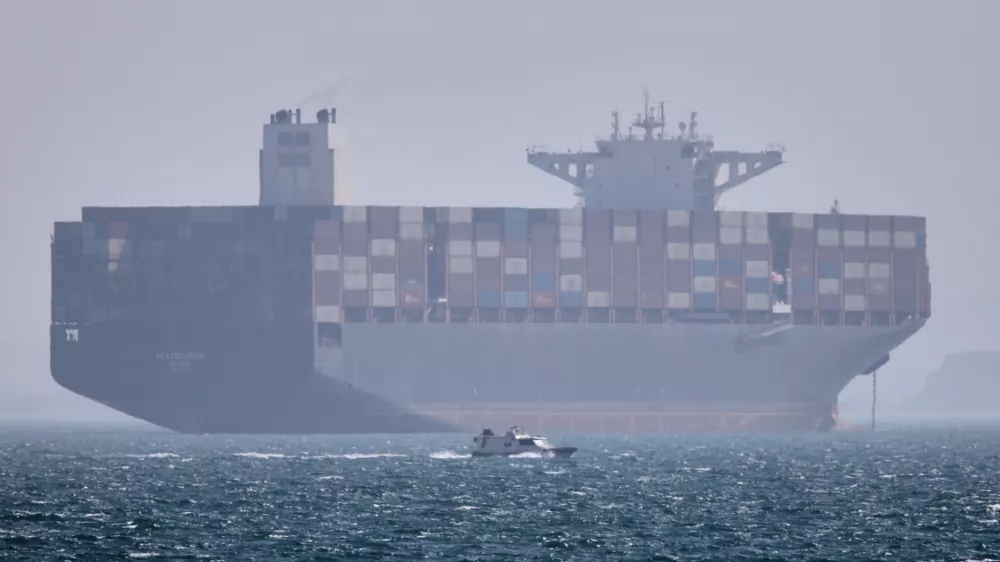 A container ship sits at anchor as a small motorboat passes in the foreground in the Strait of Hormuz off Bandar Abbas, Iran, Saturday, May 2, 2026. (Amirhosein Khorgooi/ISNA via AP)