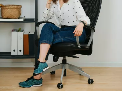 Posing woman in a desk chair at home smiling at the camera. She has her hair in a top knot, legs crossed, wearing short jeans.,Image: 718363309, License: Royalty-free, Restrictions:, Model Release: no