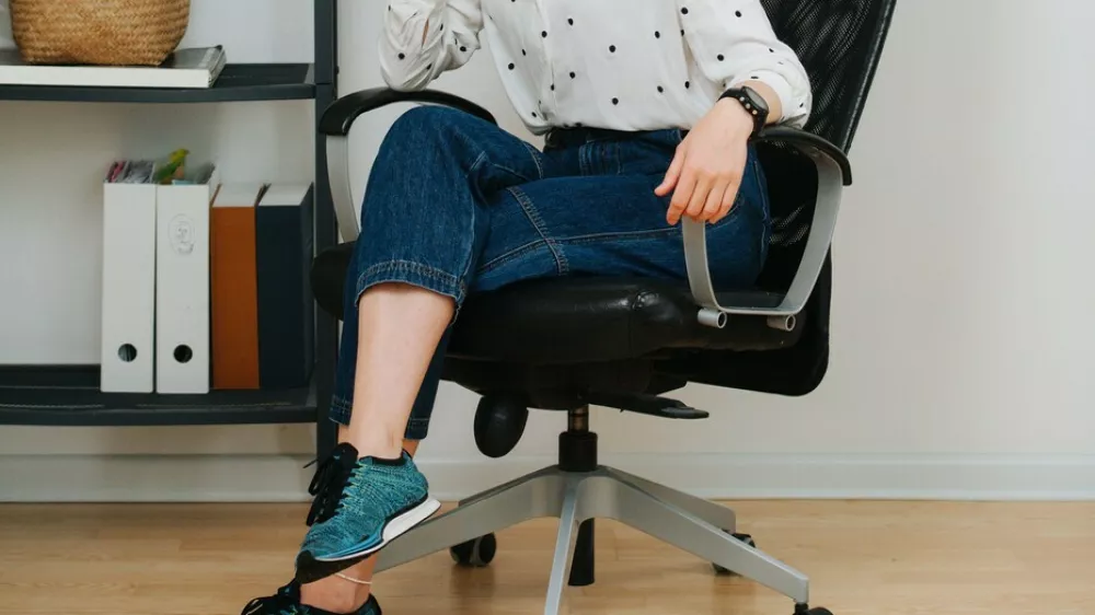 Posing woman in a desk chair at home smiling at the camera. She has her hair in a top knot, legs crossed, wearing short jeans.,Image: 718363309, License: Royalty-free, Restrictions:, Model Release: no