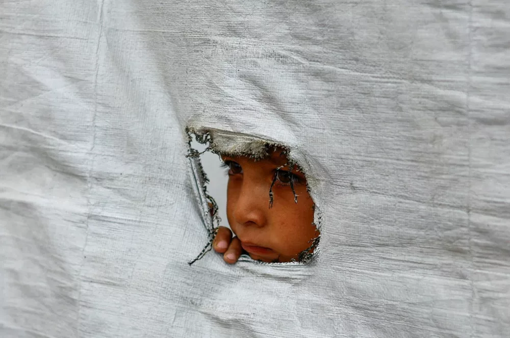 A displaced Palestinian boy peers through a tear in a tent wall, in Gaza City, May 6, 2026. REUTERS/Mahmoud Issa   TPX IMAGES OF THE DAY
