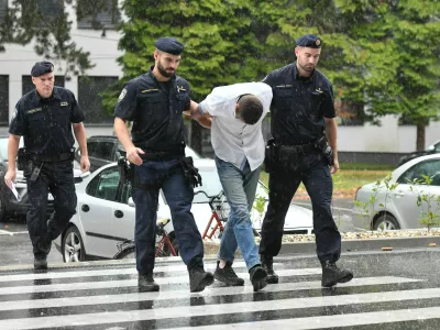 Emanuel Rep v spremstvu policistov na zasli&scaron;anje v Varaždinu. Sumijo ga umora mame s sekiro ter poskusa umorov polbrata in očima. 