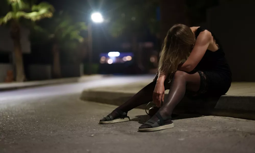 Drunk woman in dress sits on the roadside at night.